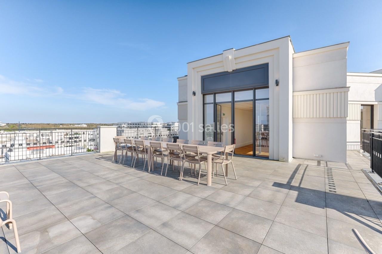 Terrasse spacieuse avec table et chaises en plein air, entourée de garde-corps, donnant sur un ciel dégagé.