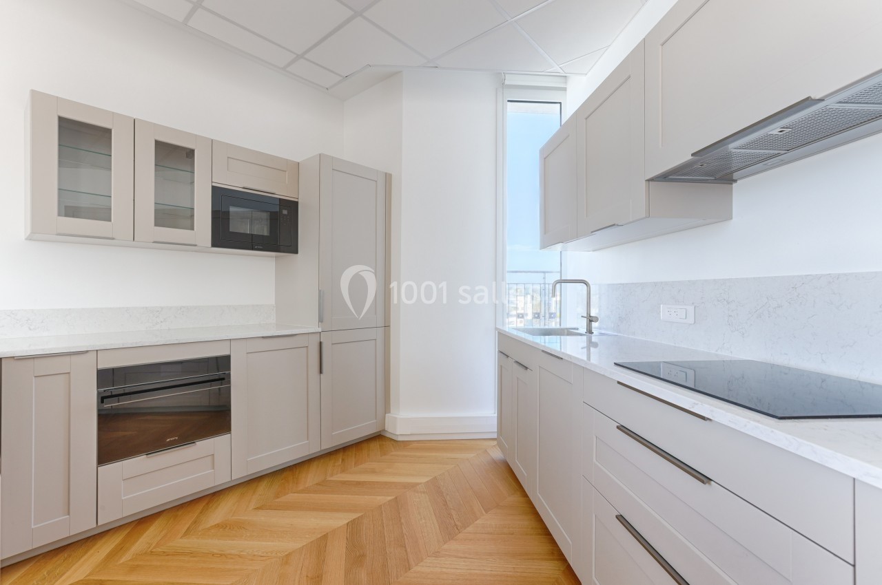 Cuisine moderne avec meubles beige clair, plan de travail en marbre, plaques de cuisson et parquet en chevrons.