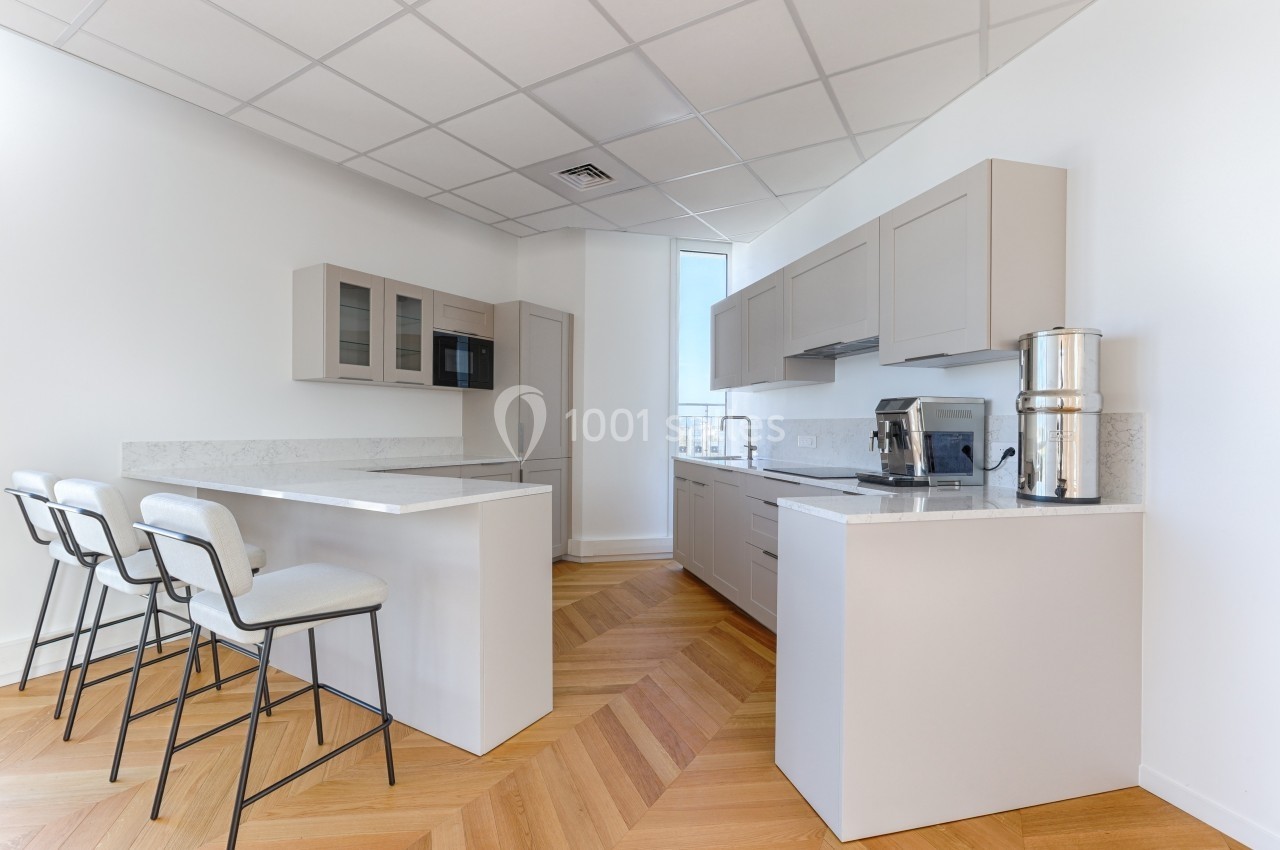 Cuisine moderne avec plancher en bois, comptoirs clairs, tabourets hauts et appareils électroménagers en inox.