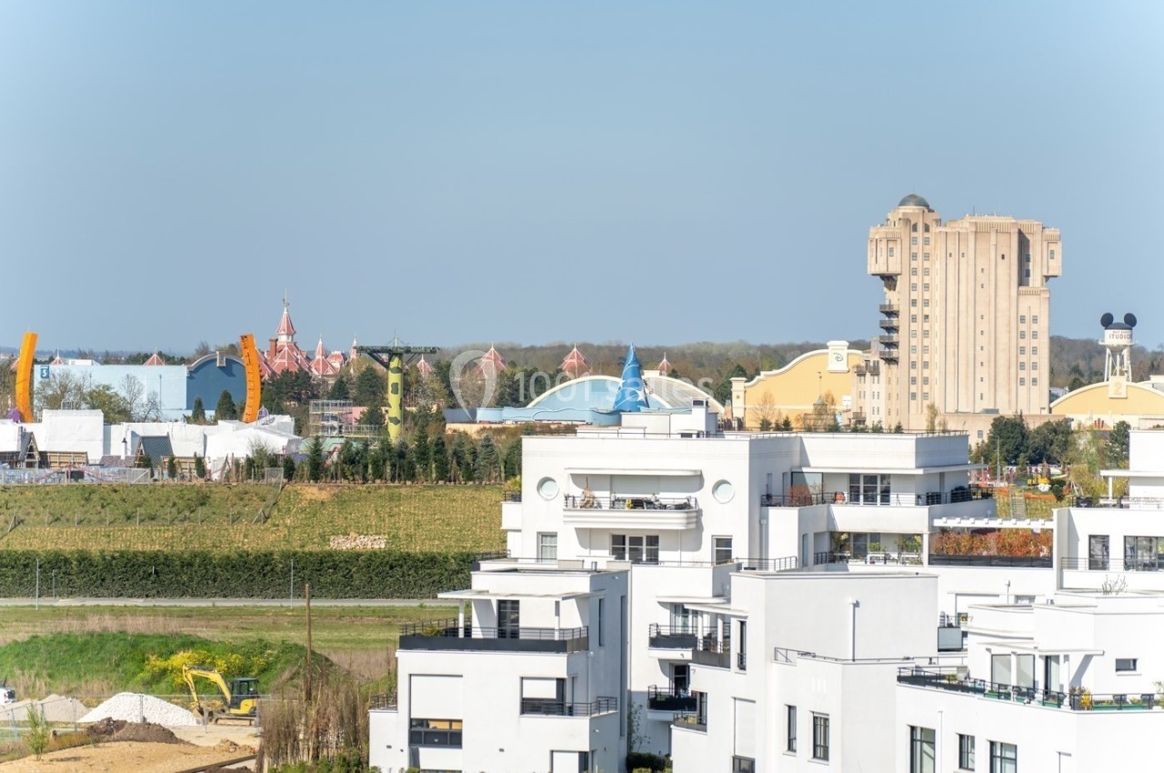 Vue sur des immeubles modernes au premier plan avec des attractions de parc à thème visibles à l'arrière-plan.