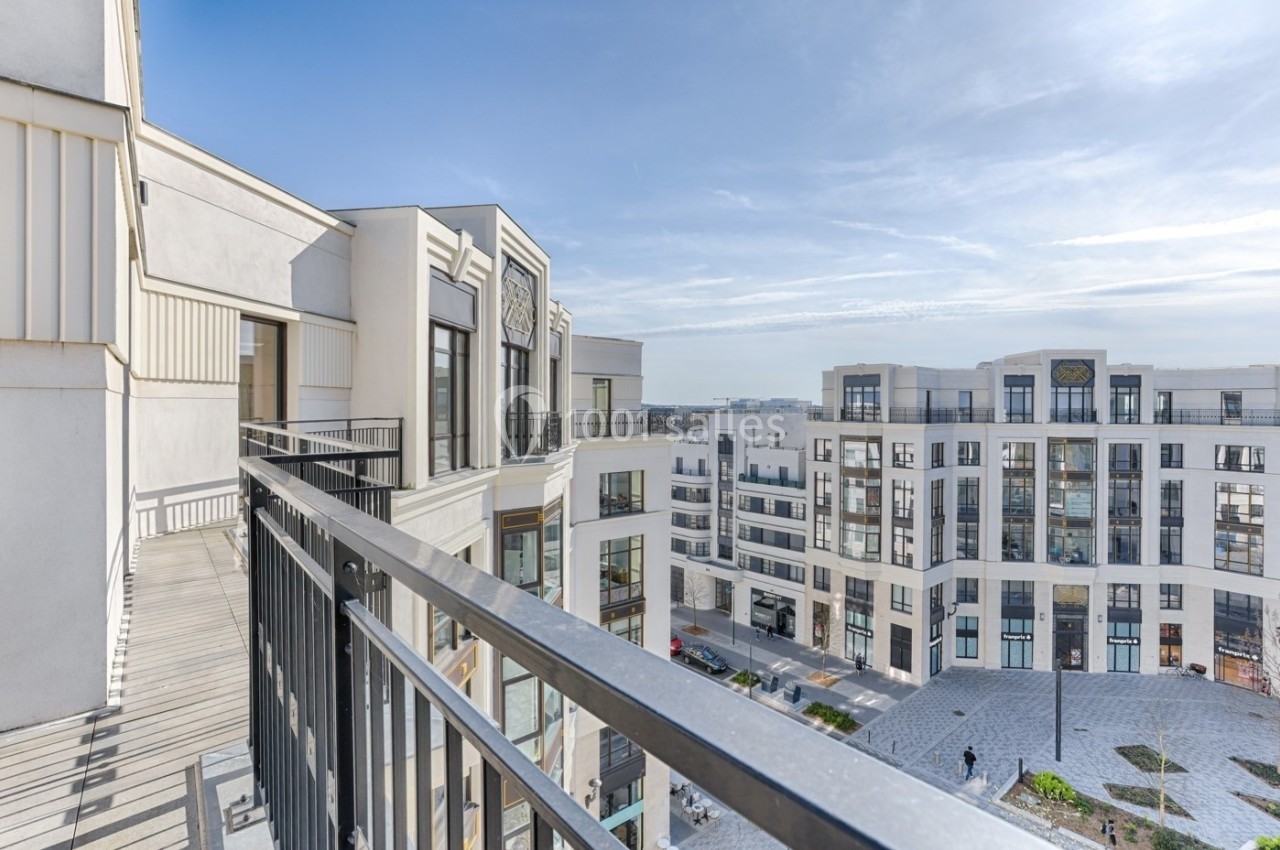 Vue depuis un balcon donnant sur une place entourée de bâtiments modernes sous un ciel dégagé.