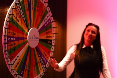 Une femme tourne une roue colorée de jeu avec des chiffres dans un environnement éclairé en rose.
