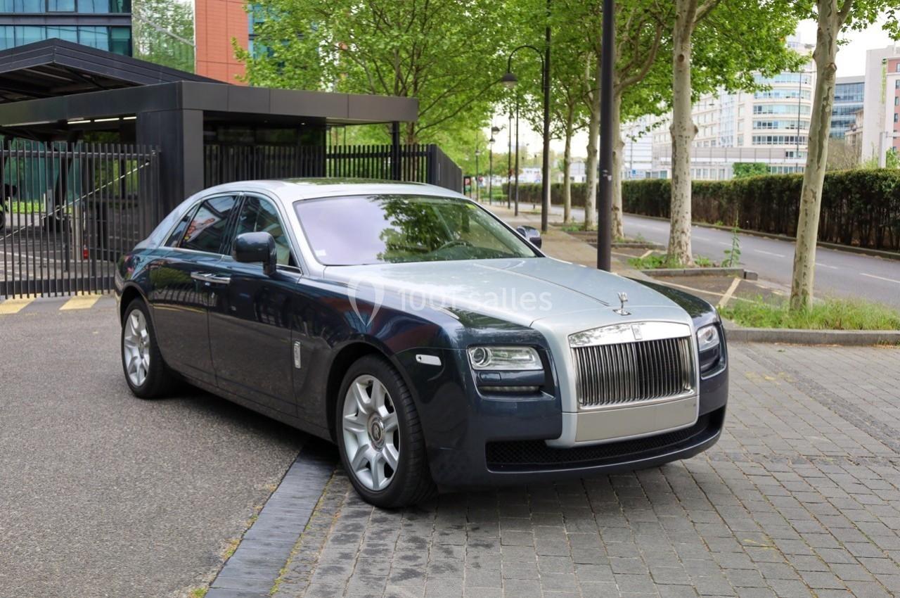 Berline de luxe gris métallisé stationnée sur une allée pavée, entourée d'arbres et de bâtiments modernes.
