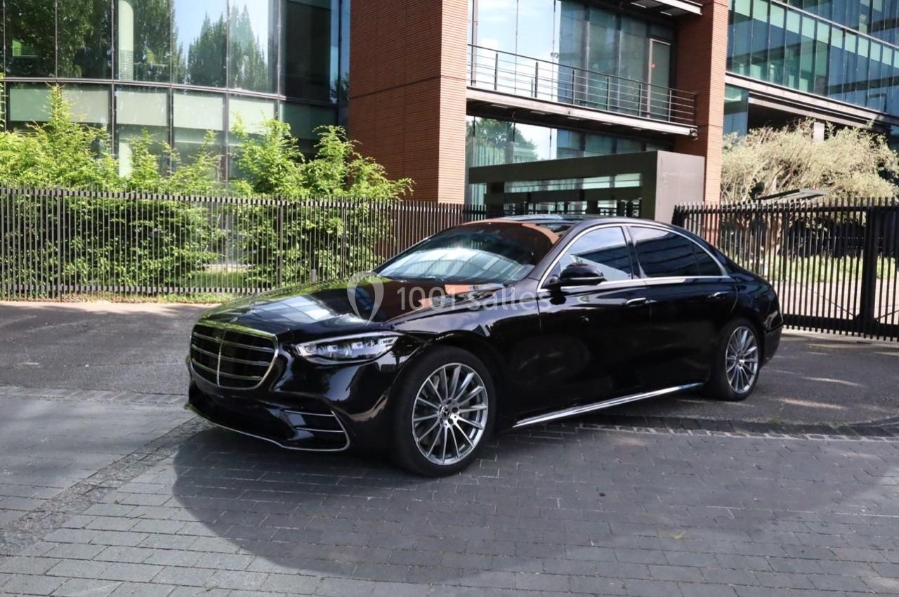 Voiture noire garée devant un bâtiment moderne avec des façades vitrées et des arbres en arrière-plan.
