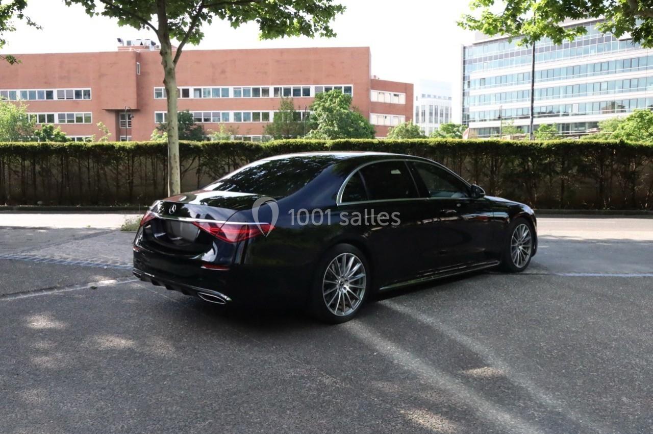 Voiture noire stationnée sur un parking, entourée de bâtiments modernes et d'arbres.