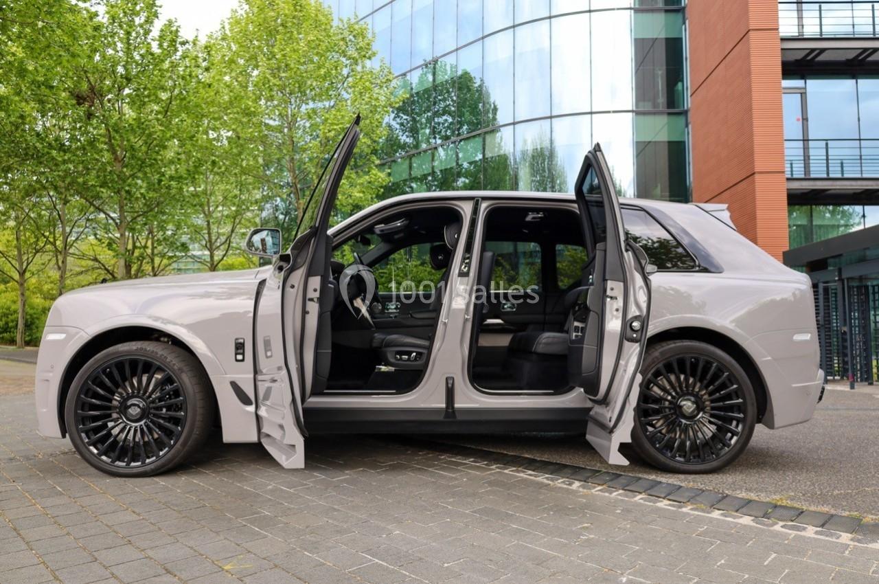 SUV gris avec portes ouvertes, stationné devant un bâtiment moderne entouré d'arbres et de vitrages.