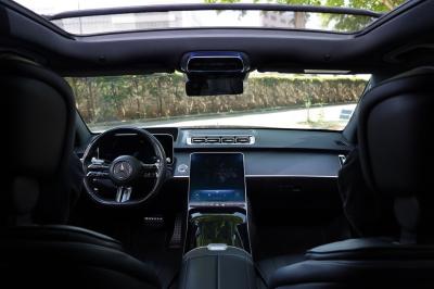 Voiture de luxe grise avec portes ouvertes, intérieur beige, stationnée devant un bâtiment moderne vitré.