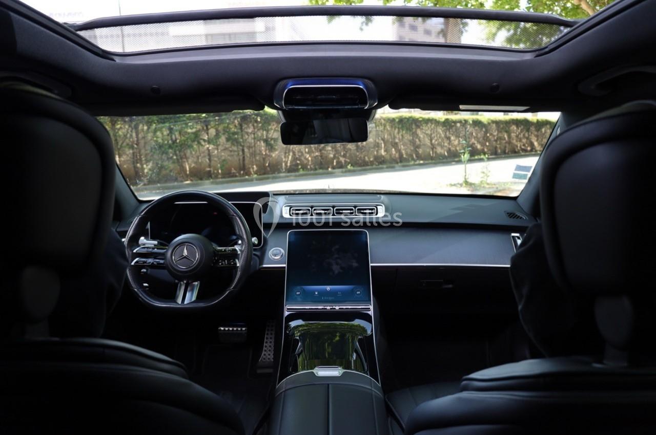 Vue intérieure d'une voiture haut de gamme avec tableau de bord moderne, écran central et toit panoramique.