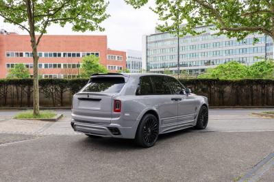 Voiture de luxe grise avec portes ouvertes, intérieur beige, stationnée devant un bâtiment moderne vitré.