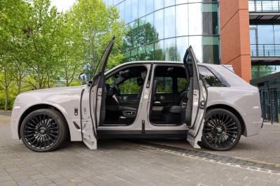 Voiture de luxe grise avec portes ouvertes, intérieur beige, stationnée devant un bâtiment moderne vitré.