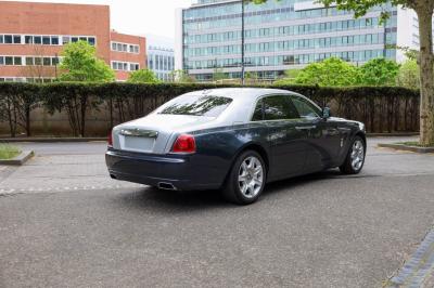 Voiture de luxe grise avec portes ouvertes, intérieur beige, stationnée devant un bâtiment moderne vitré.