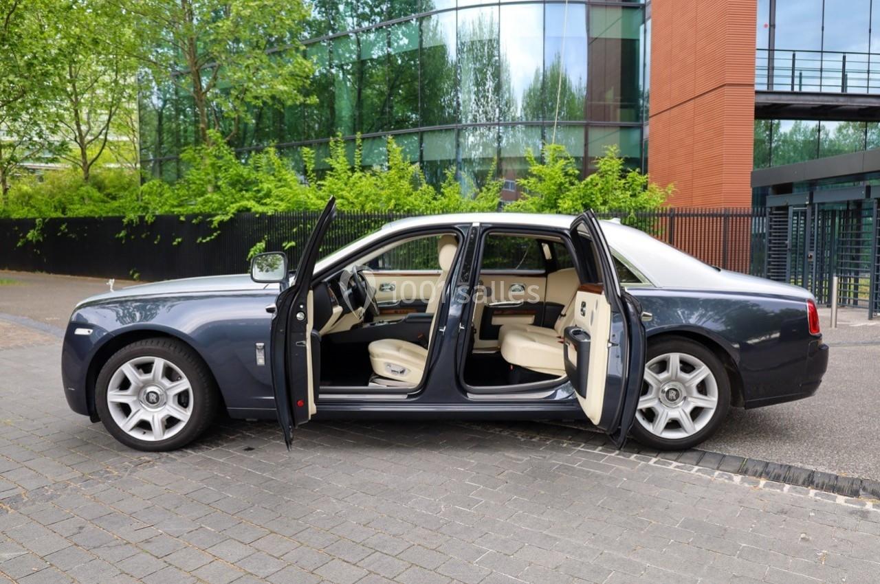 Voiture de luxe grise avec portes ouvertes, intérieur beige, stationnée devant un bâtiment moderne vitré.