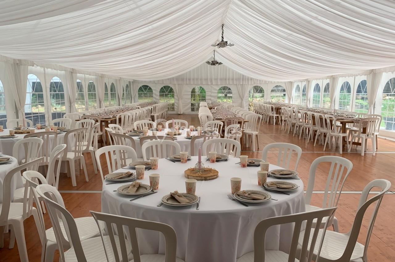 Salle de réception sous chapiteau blanc avec tables rondes et rectangulaires dressées pour un événement.
