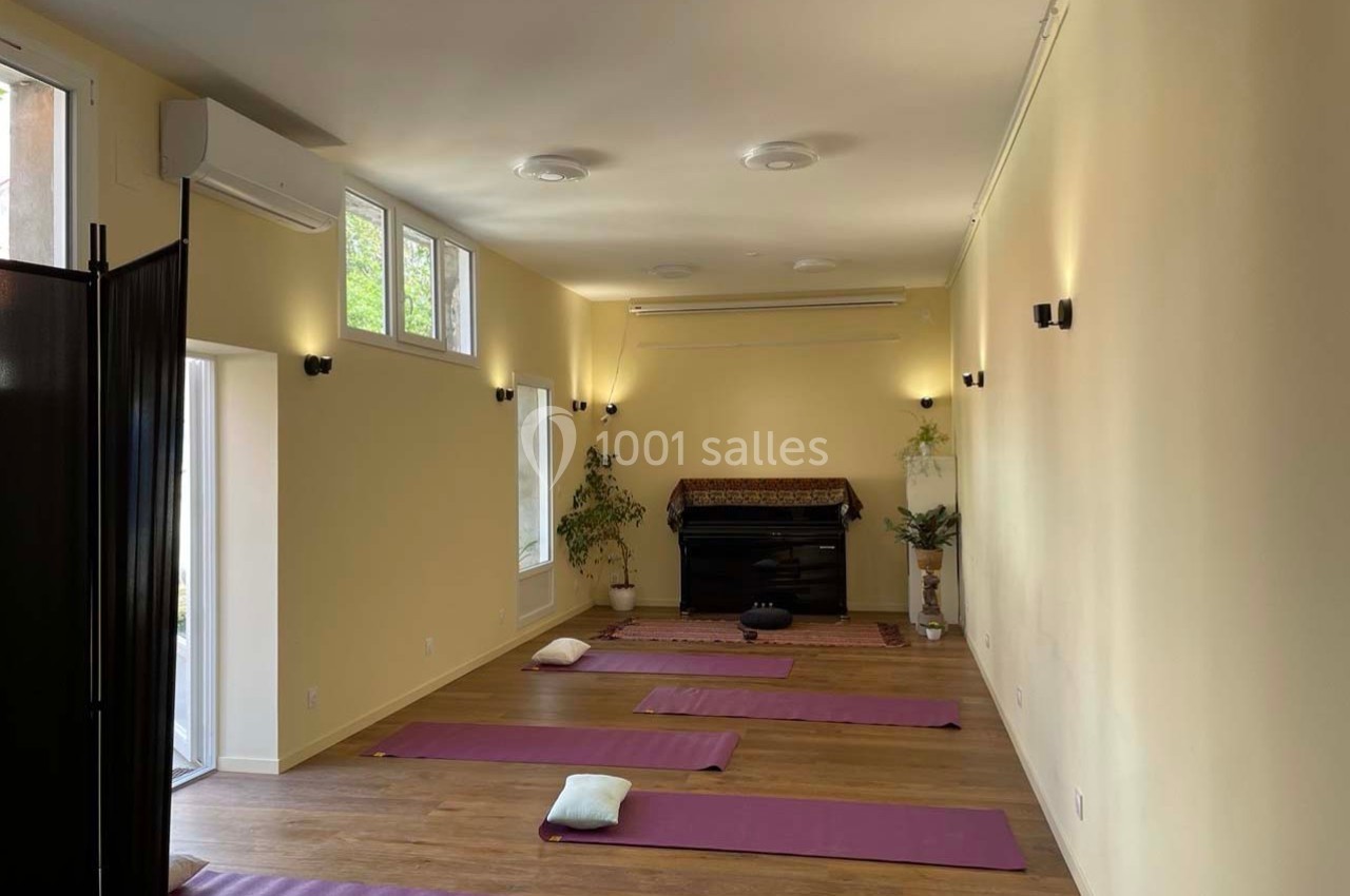 Salle lumineuse avec des tapis de yoga alignés sur un sol en bois, entourée de murs jaunes et de plantes décoratives.