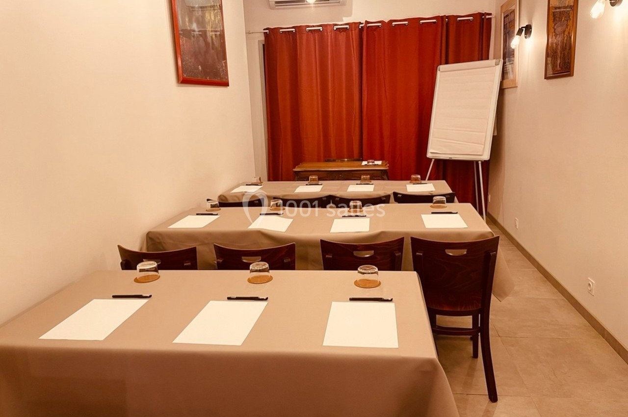 Salle de réunion avec tables alignées, chaises, blocs-notes, stylos, verres et un tableau de présentation devant des rideaux…