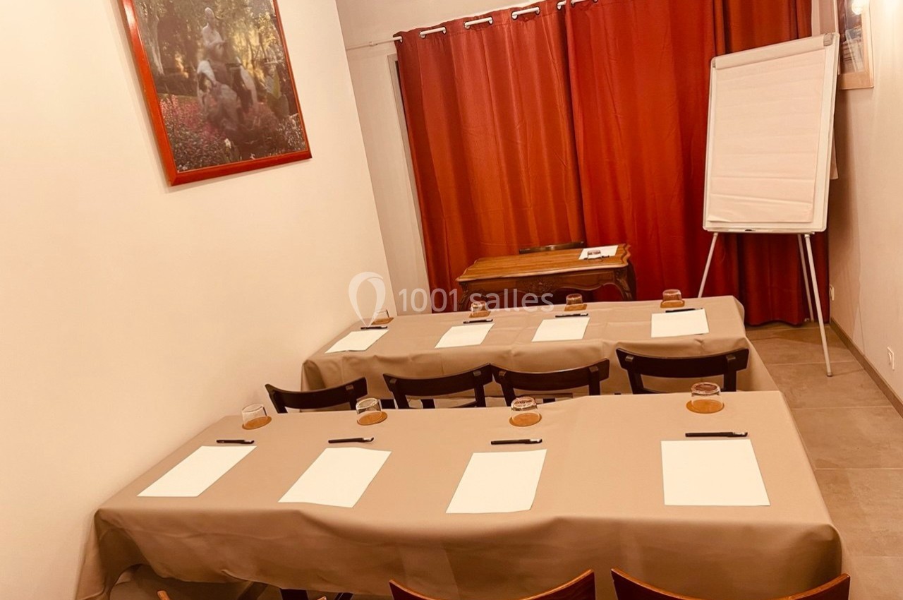 Salle de réunion avec tables disposées en rangées, blocs-notes et stylos, tableau blanc et rideaux rouges en arrière-plan.