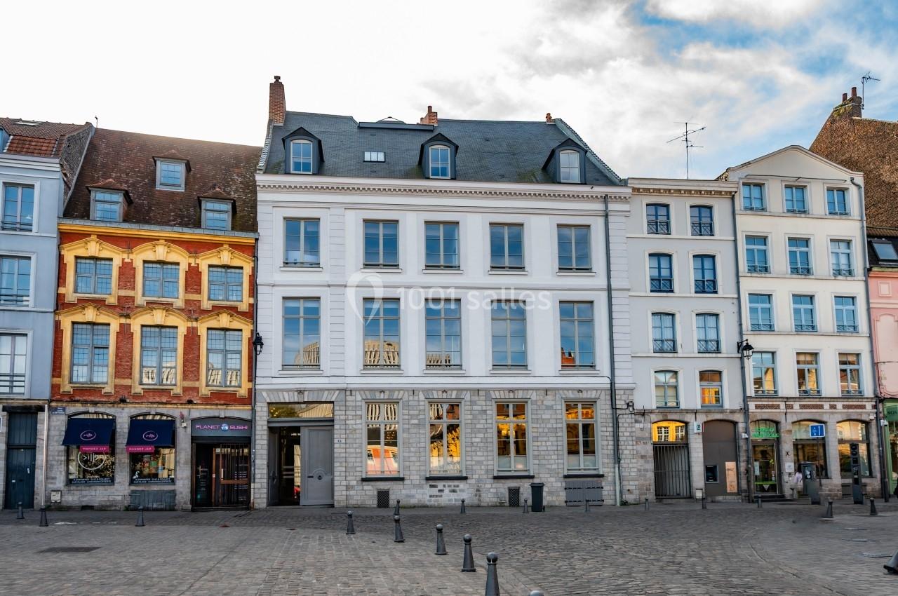 Façade de maisons colorées et bâtiments anciens alignés sur une place pavée sous un ciel partiellement nuageux.