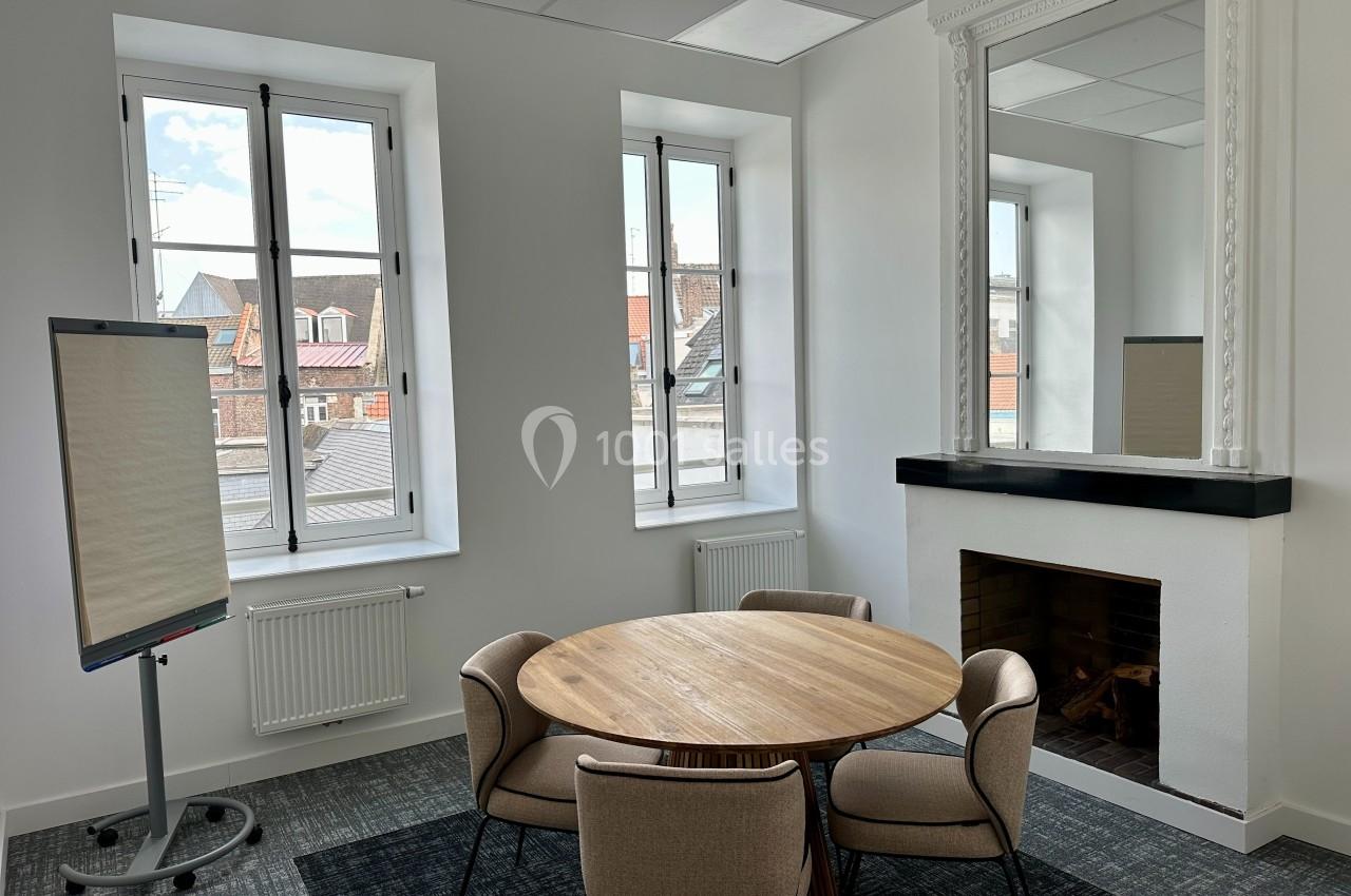 Salle de réunion lumineuse avec table ronde, quatre chaises, un paperboard et une cheminée décorative.