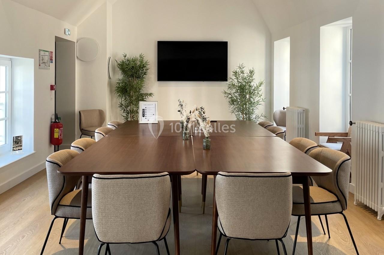 Salle de réunion lumineuse avec une grande table en bois entourée de chaises et des poutres apparentes au plafond.