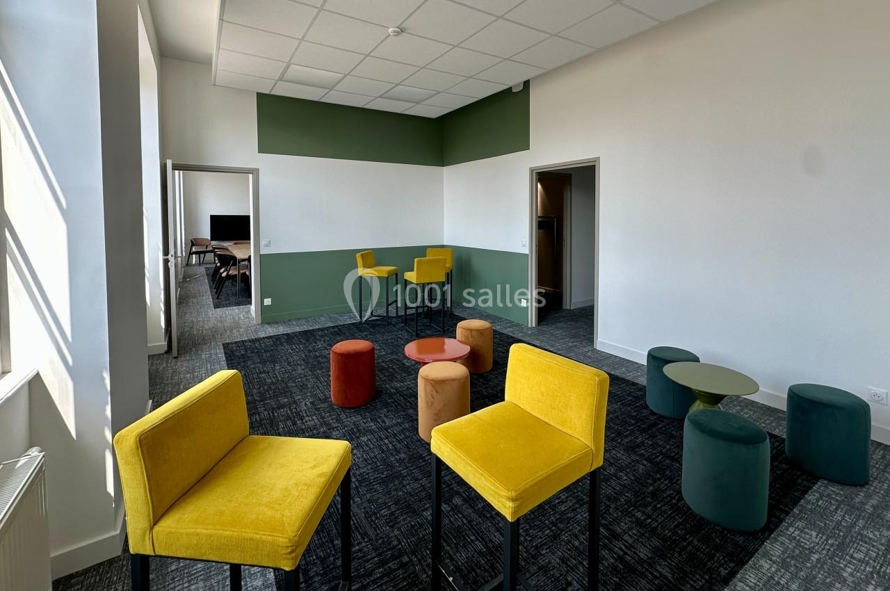 Salle lumineuse avec chaises jaunes, tabourets colorés et tables basses, décorée de murs blancs et verts.