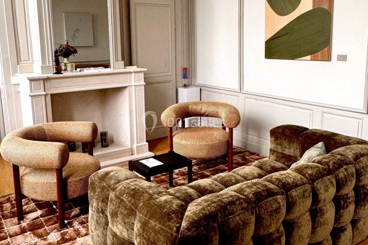 Salon élégant avec canapé en velours, fauteuils assortis, cheminée blanche et tableau abstrait sur un mur boisé.