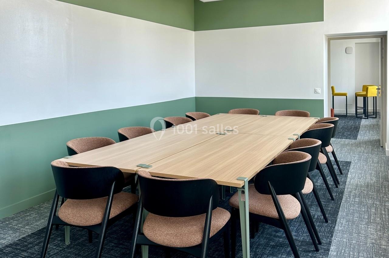 Salle de réunion avec une grande table en bois entourée de chaises, éclairée par une lumière naturelle.