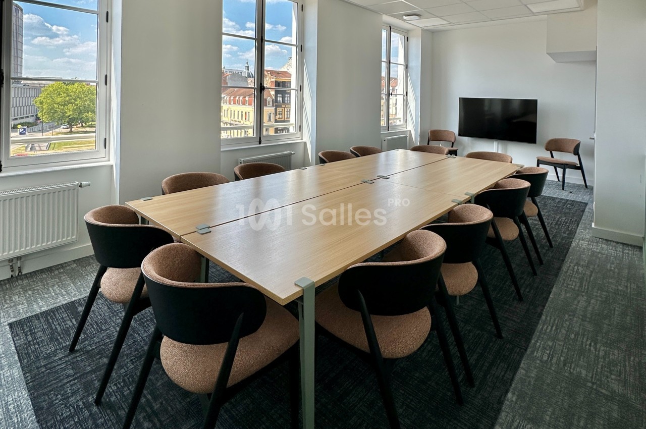 Salle de réunion lumineuse avec une grande table en bois entourée de chaises, fenêtres donnant sur un paysage urbain.