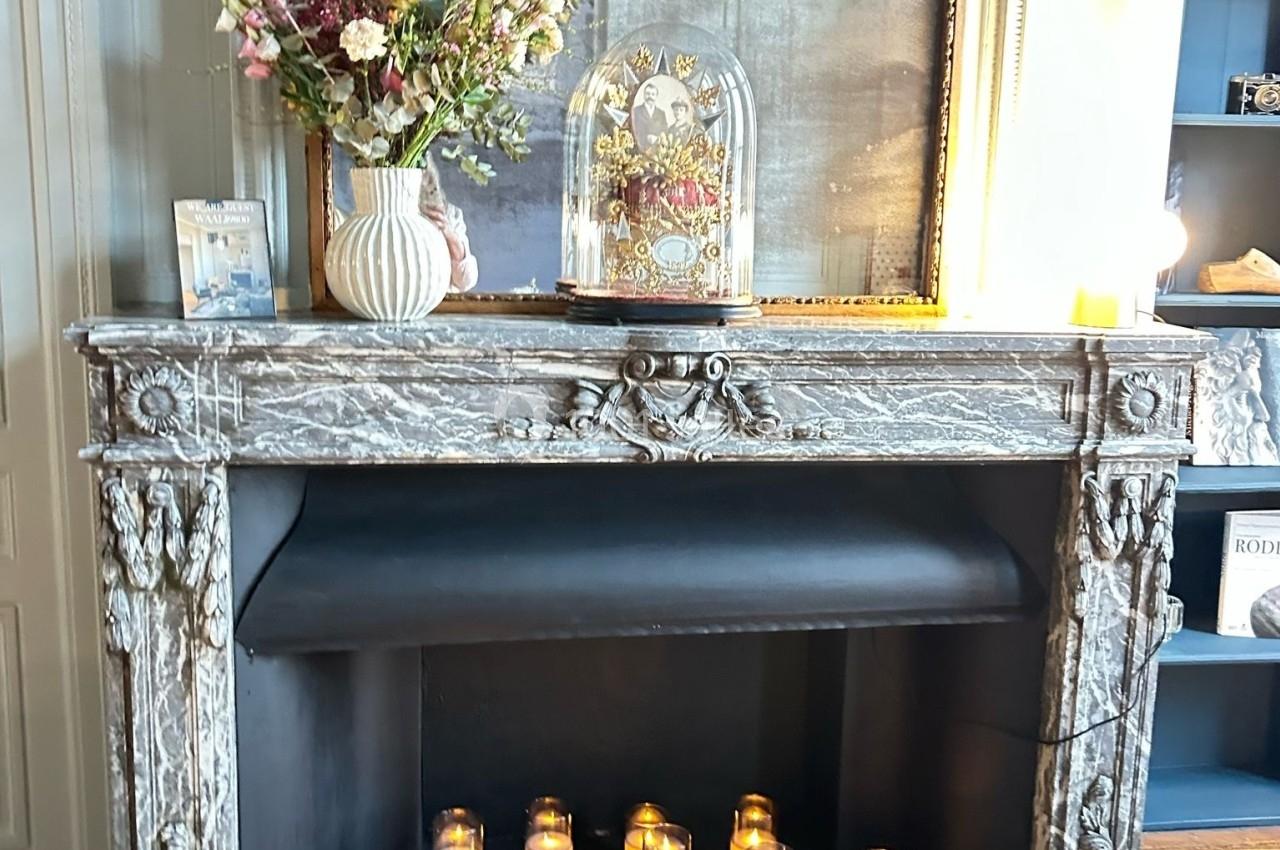 Cheminée en marbre gris décorée de bougies allumées, d'un bouquet de fleurs et d'une cloche en verre.