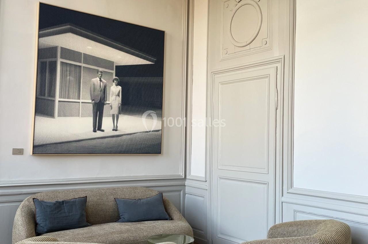 Salon lumineux avec deux fauteuils et un canapé beige sur un tapis clair, décoré d'un tableau moderne et d'un luminaire…