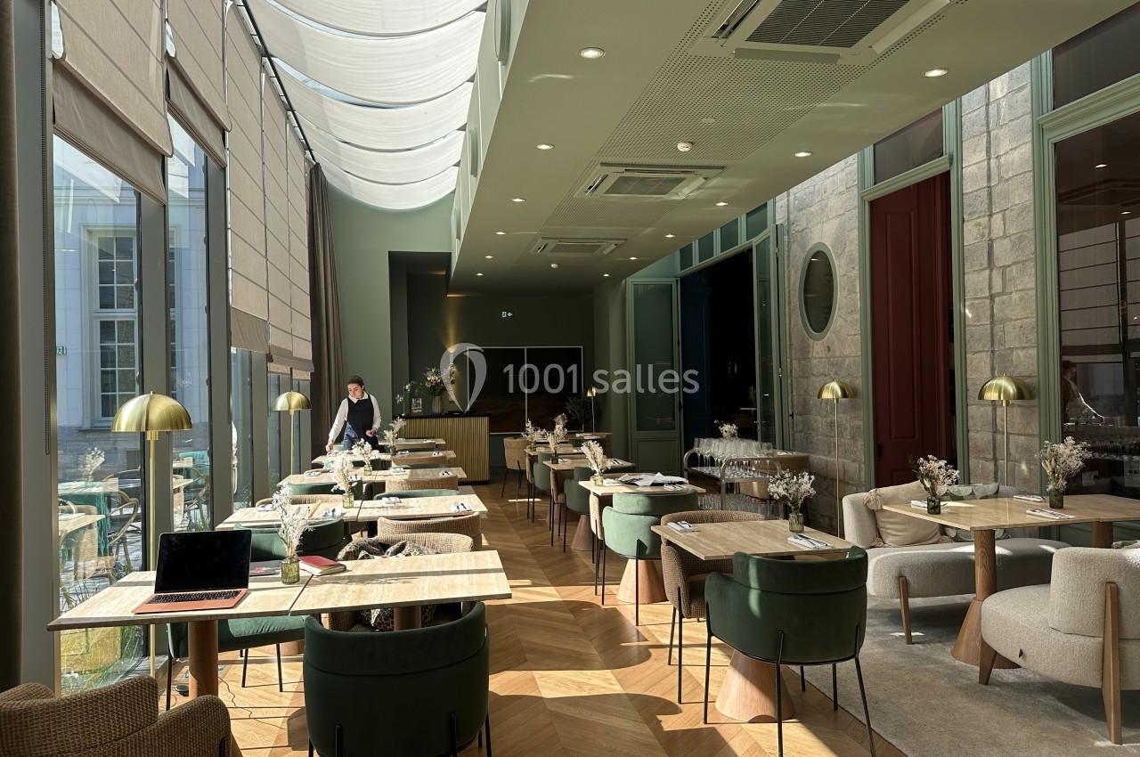 Salle de restaurant lumineuse avec de grandes baies vitrées, tables dressées et décoration moderne.