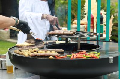 Deux personnes cuisinent des légumes colorés sur une grande plancha en extérieur, par une journée ensoleillée.