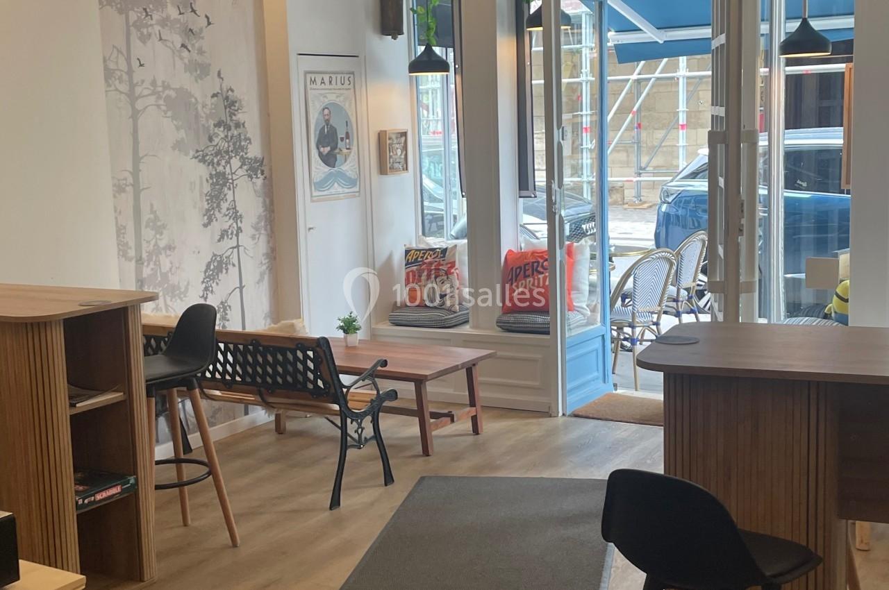 Intérieur d'un café moderne avec mobilier en bois, grandes fenêtres et décoration murale minimaliste.