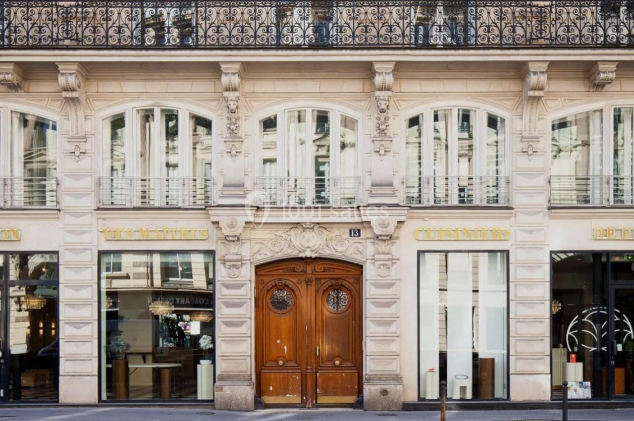 Façade d'un immeuble haussmannien avec une porte en bois centrale et des vitrines commerciales de part et d'autre.