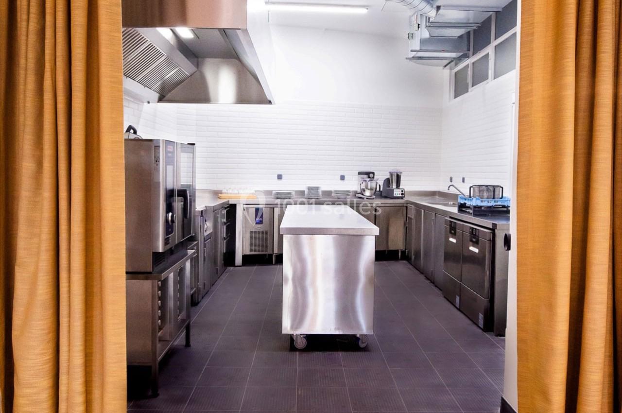 Cuisine professionnelle équipée avec plan de travail en inox, appareils de cuisson et murs carrelés blancs.