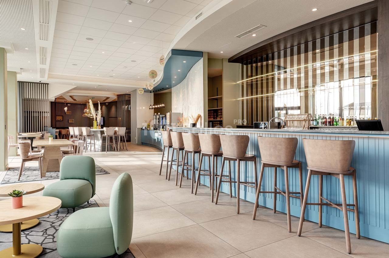 Intérieur d'un bar moderne avec comptoir bleu, tabourets hauts, tables basses et décoration lumineuse.