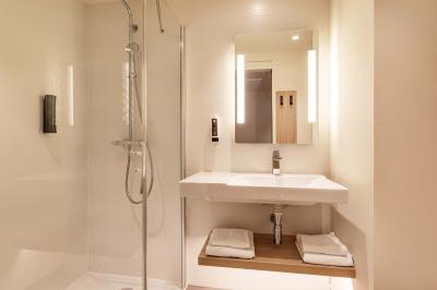 Salle de bain moderne avec douche à l'italienne, lavabo avec miroir éclairé et serviettes pliées sur une étagère.