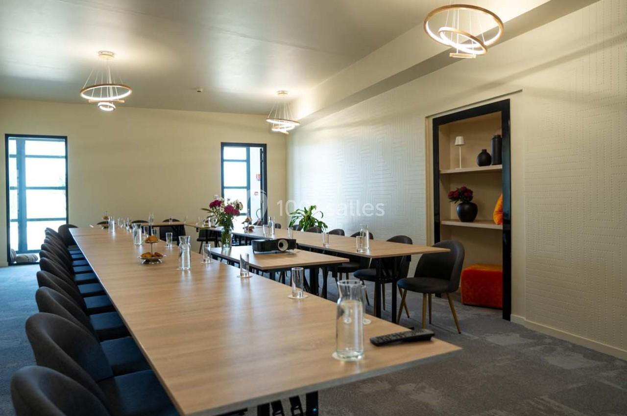 Salle de réunion lumineuse avec une longue table en bois, des chaises noires, des bouteilles d'eau et des décorations…