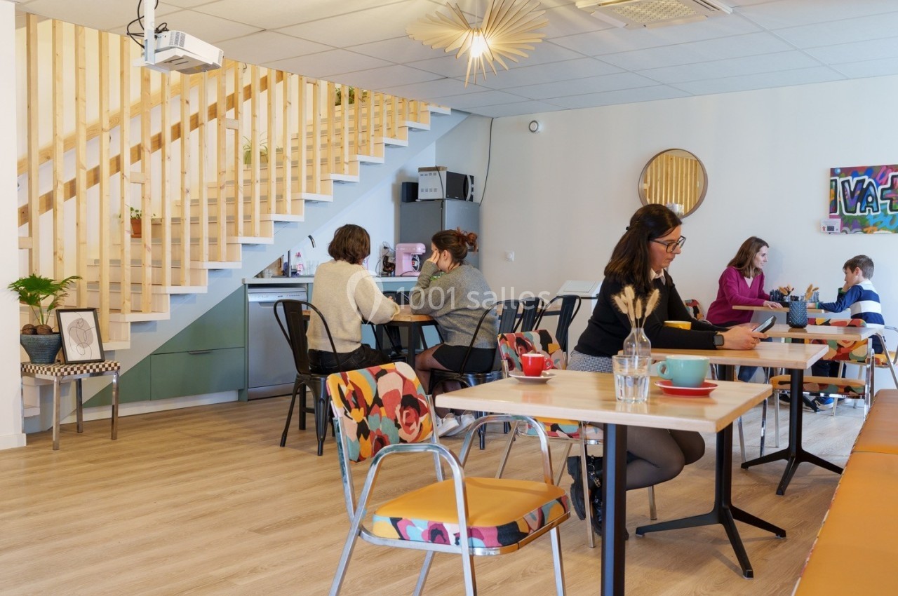Espace de coworking lumineux avec des personnes travaillant à des tables, escalier en bois en arrière-plan.
