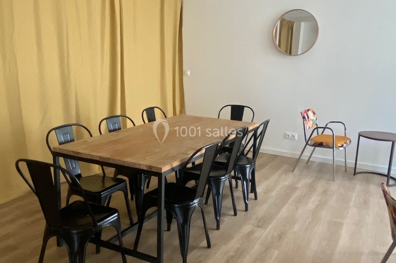 Salle à manger avec table en bois, chaises noires, rideaux jaunes, miroir rond et sol en parquet clair.