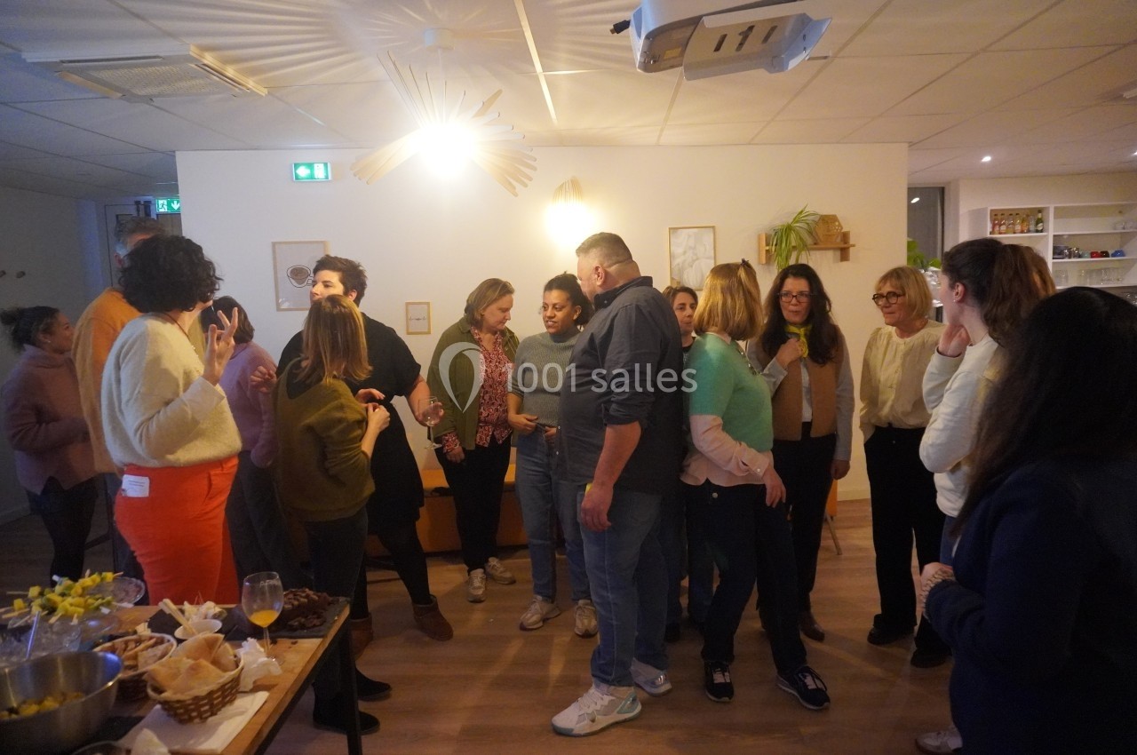 Groupe de personnes discutant dans une salle lumineuse avec des décorations murales et des tables garnies.