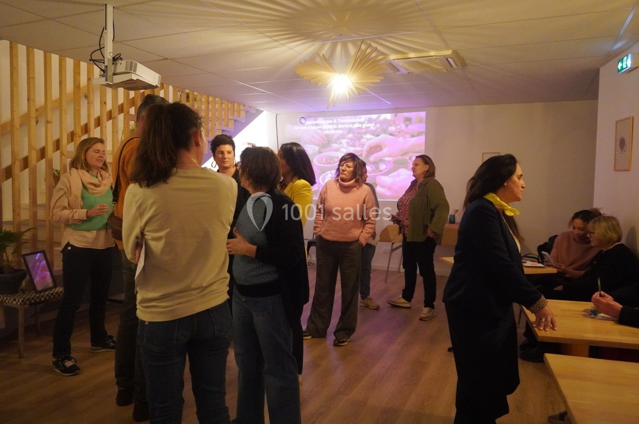 Des personnes discutent dans une salle lumineuse avec un projecteur affichant une image en arrière-plan.