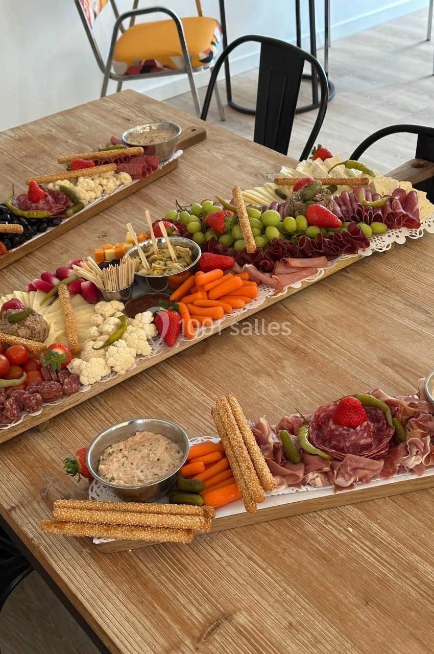 Plateaux de charcuterie et crudités variés avec fruits, légumes, fromages et dips sur une table en bois.