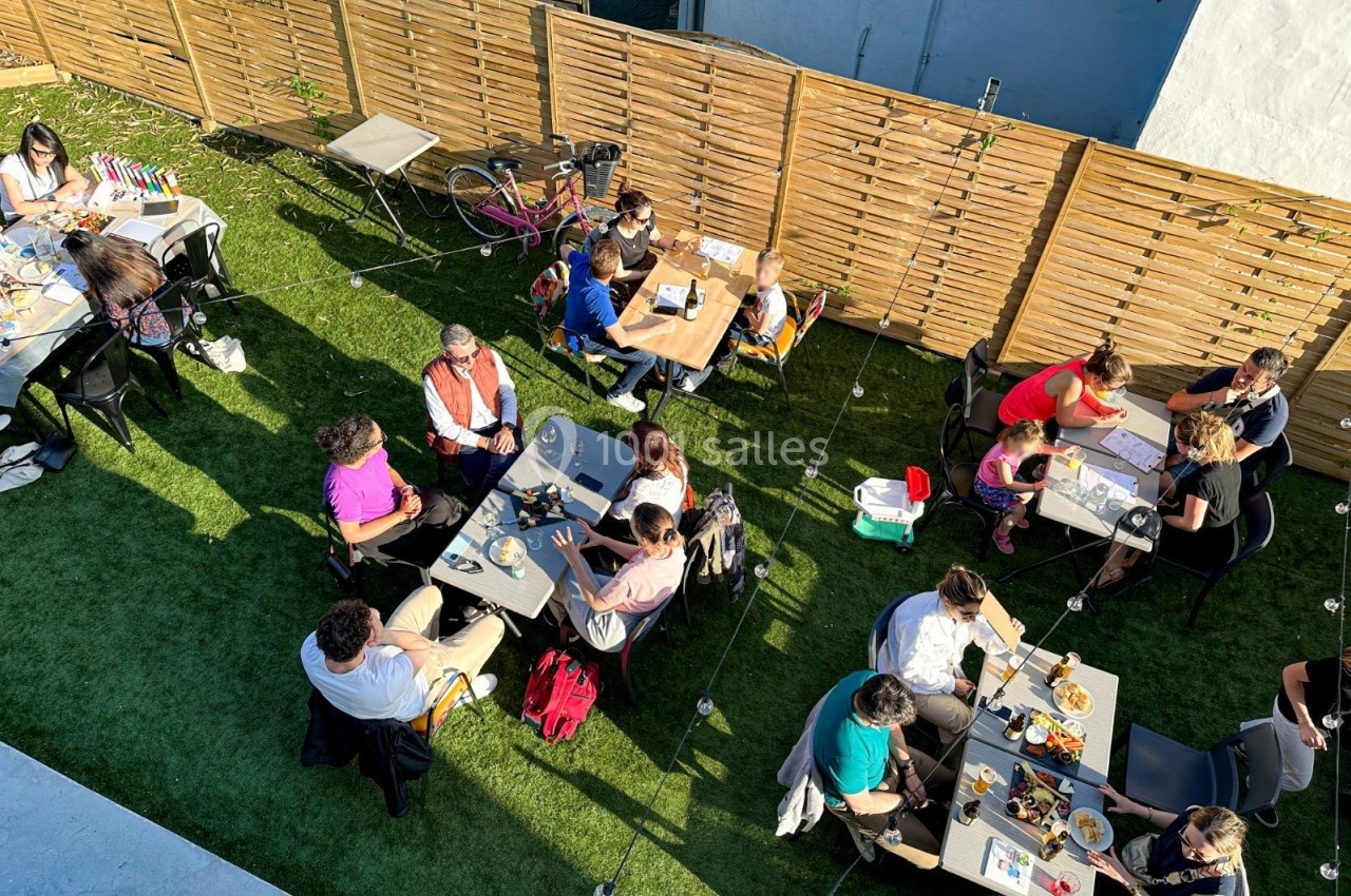 Vue aérienne d'une terrasse extérieure avec des personnes assises à des tables, partageant des repas et des conversations.