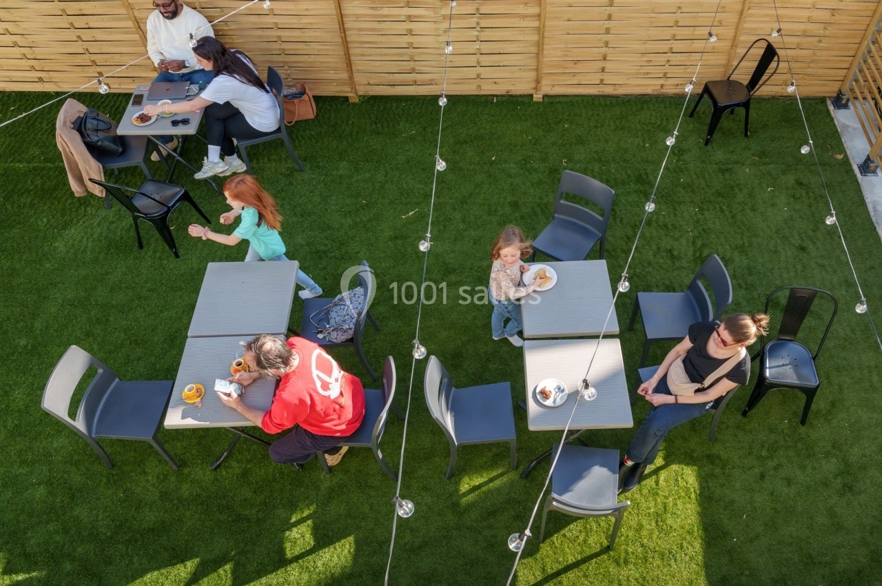 Des personnes assises et debout dans un espace extérieur avec des tables, des chaises et un sol en gazon artificiel.