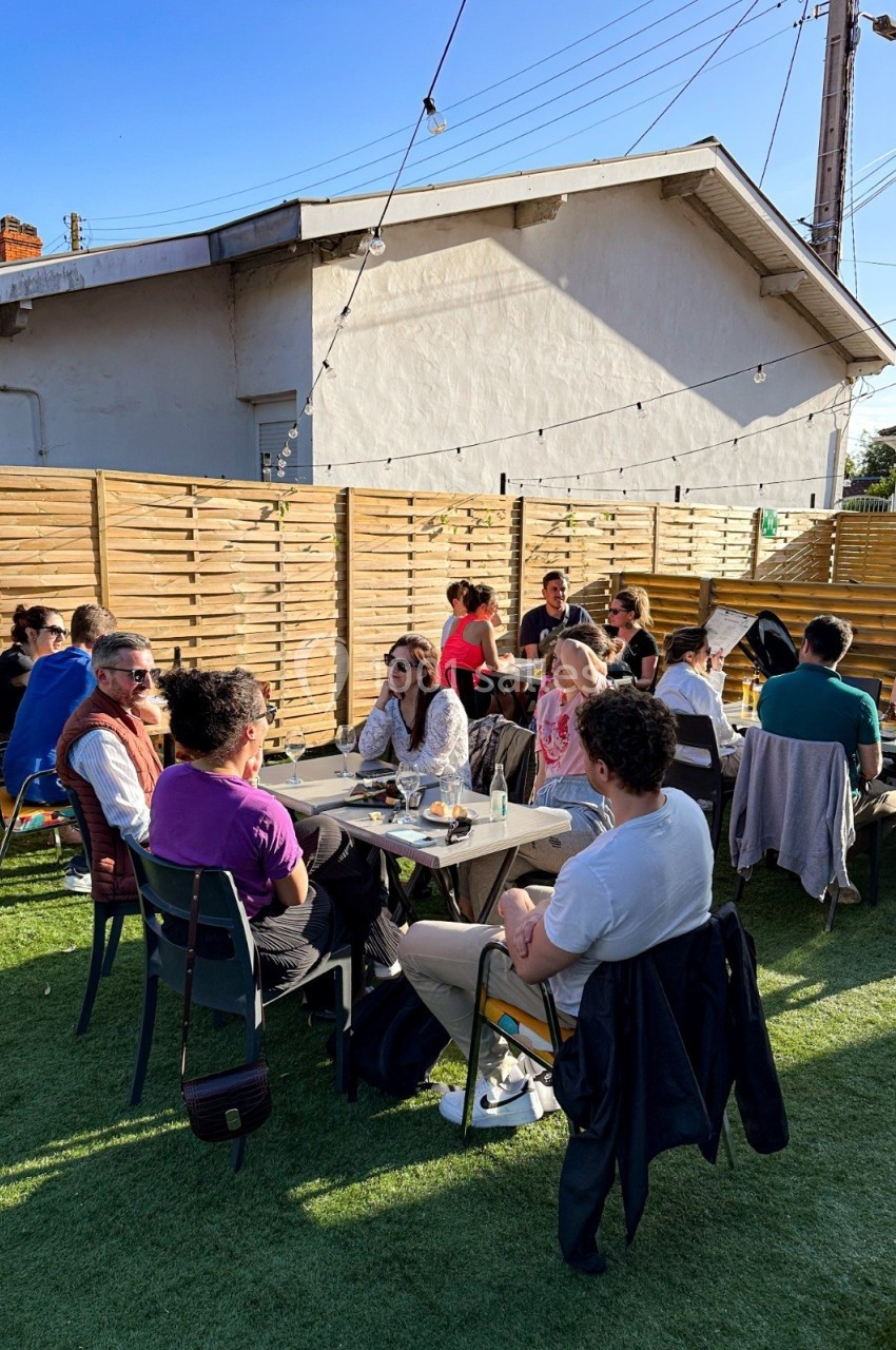 Personnes assises autour de tables en extérieur, discutant et partageant un moment convivial sous un ciel dégagé.