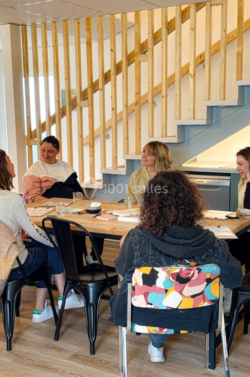 Quatre personnes discutent autour d'une table dans un espace intérieur lumineux avec un escalier en arrière-plan.