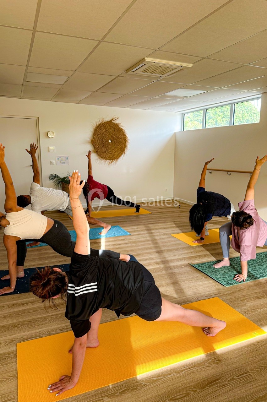 Un groupe de personnes pratique le yoga dans une salle lumineuse, effectuant une posture d'étirement latéral.