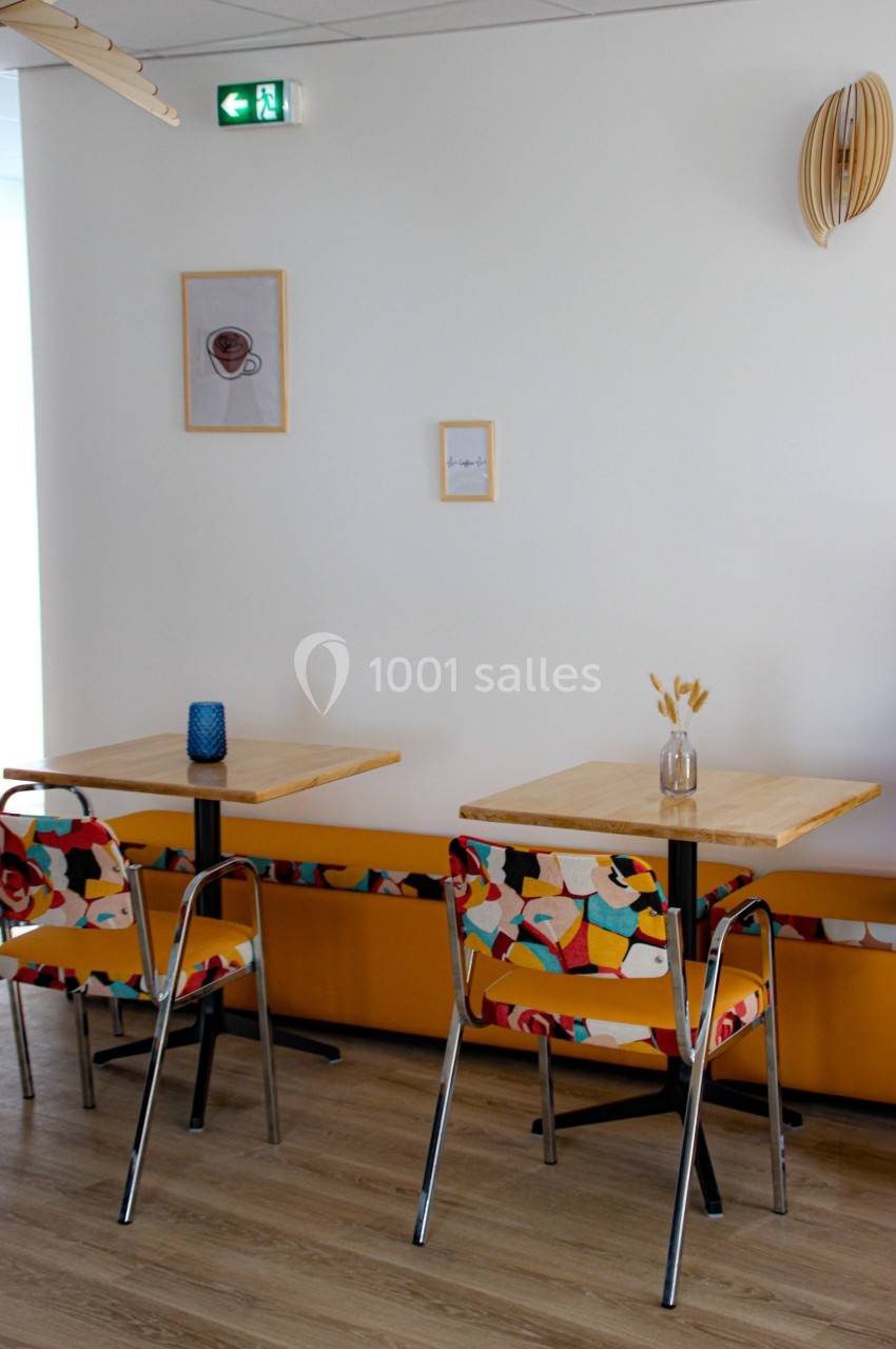 Deux tables avec chaises colorées dans un intérieur lumineux, décoré de cadres et d'objets muraux.
