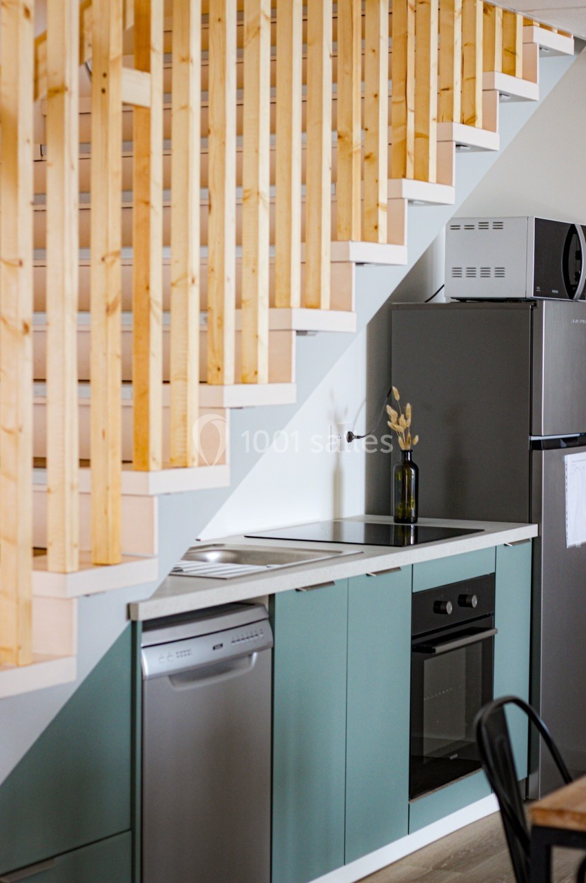 Cuisine compacte sous un escalier en bois, équipée d'un four, d'un lave-vaisselle, d'un réfrigérateur et d'un plan de…