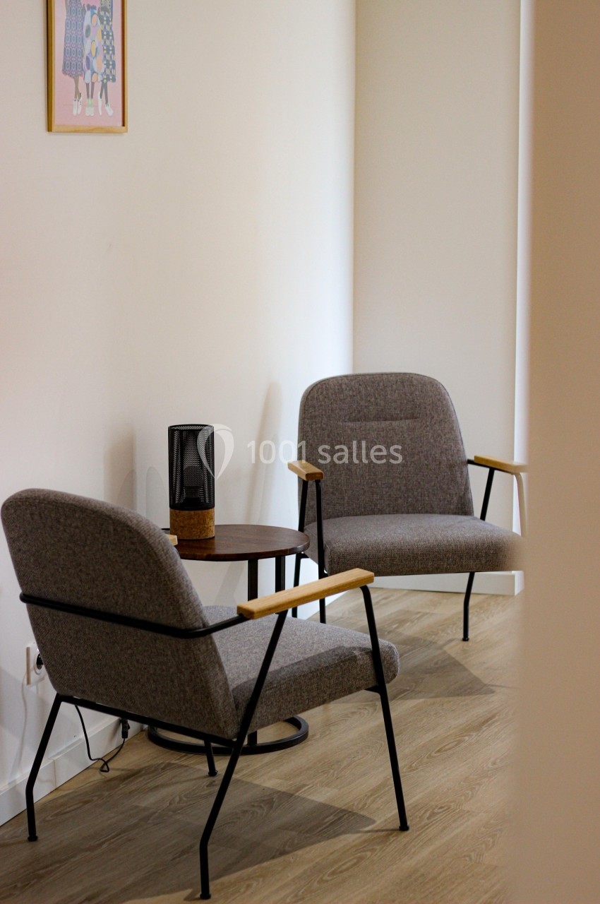 Deux fauteuils gris avec accoudoirs en bois autour d'une petite table dans un intérieur lumineux.